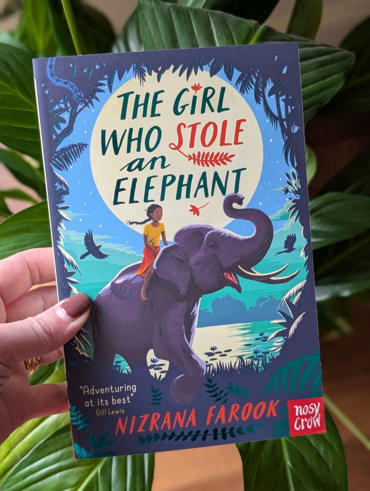 A brightly coloured children's book with an elephant and a girl sitting on top of it taking centre stage. Birds, clouds, blue sky and foliage make up the background images 