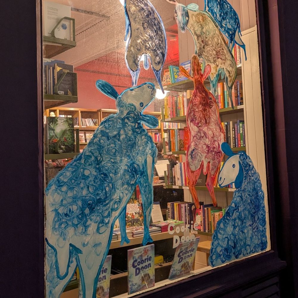 A book shop window. The glass has been painted with blue and red animals. The book on shelves behind it 