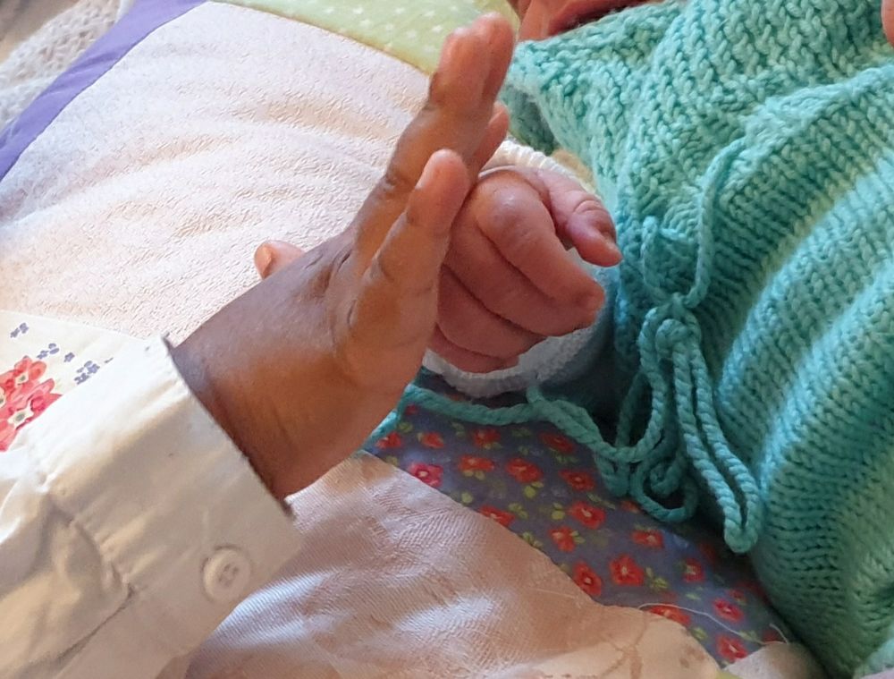 Kleinkindhand berührt sanft die Hand eines Säuglings.