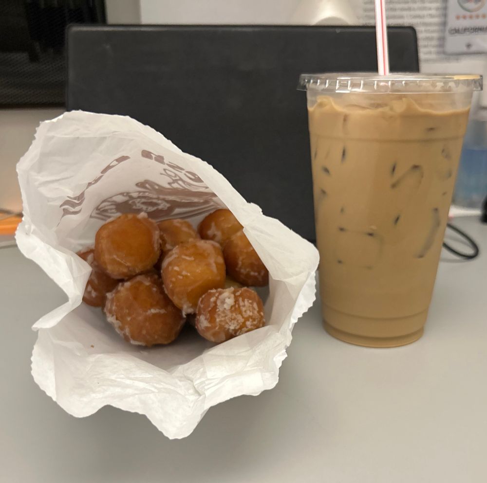 Photo of a bag of donut holes next to a large Vietnamese coffee that is strong enough to make you see into the future. 