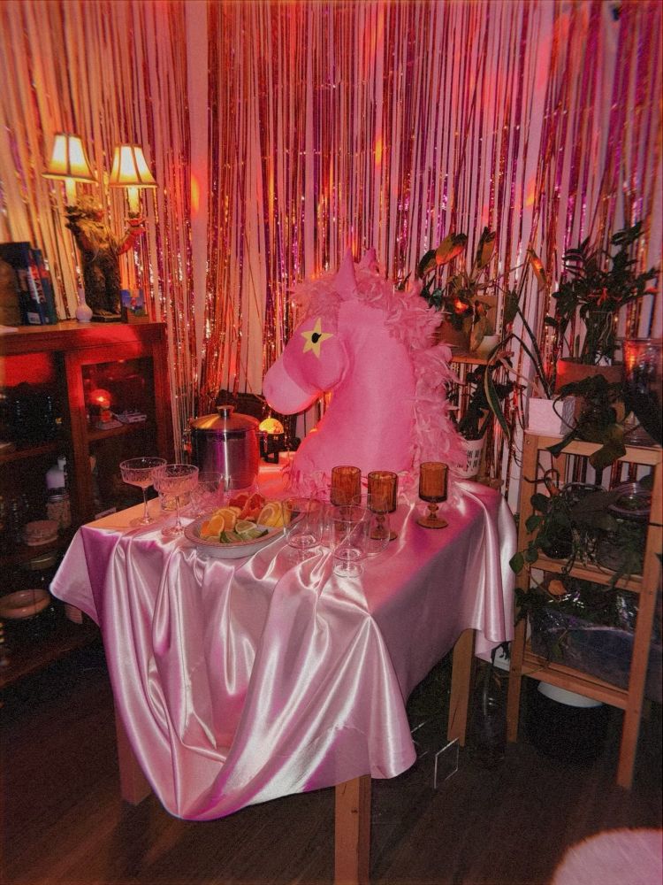 A table with a big pink pony head, cocktail glasses and sliced citrus with a shiny pink table cloth