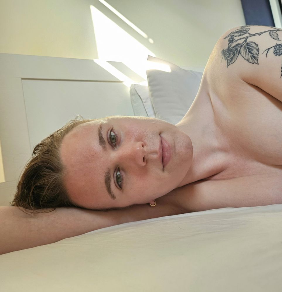 Woman laying in bed on her side with her head on her arm. Decolletage visible with some extremely contrived cleavage from laying sideways and squishing a boob with her upper arm. 