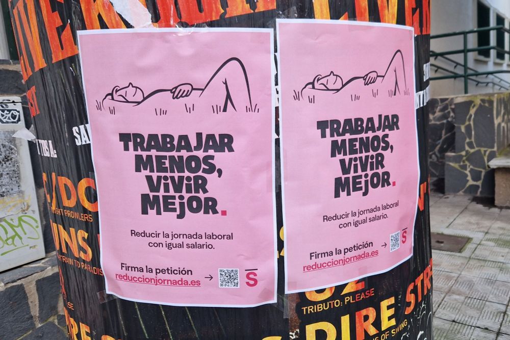 Carteles pegados con el lema "Trabajar menos, vivir mejor" y el texto: "Reducir la jornada laboral con igual salario, firma la petición en reduccionsalario.es"