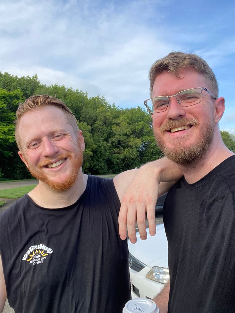 Two men smiling at the camera post run, one is leaning on the others shoulder. 