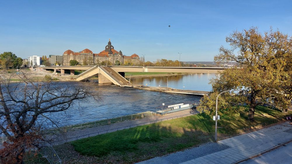 Blick auf die Elbe in Dresden, über den Fluss führt die Carolabrücke. Der vordere Teil ist eingestürzt und die Fahrbahnen liegen rechts und links von einem Pfeiler schräg ins Wasser. Der rechte Teil der Fahrbahn liegt flach in der Elbe.