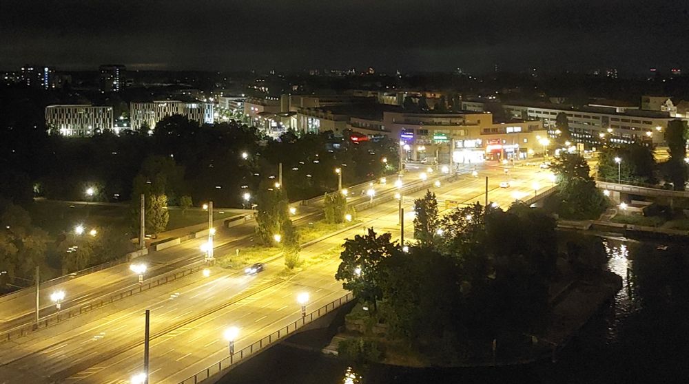 Nachts eine leere mehrspurige Straße von schräg oben aufgenommen. Die Straßenlaternen tauchen die Fahrbahnen in ein goldenes Licht. 