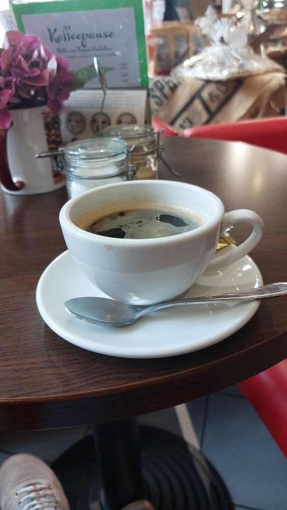 Auf einem runden braunen Holztisch steht eine weiße Porzellantasse auf einer weißen Untertasse. In der Tasse ist ein Cafè crema.