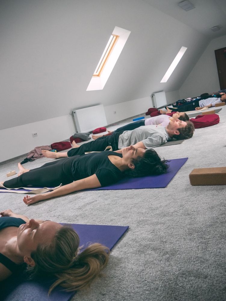 Karolina laying down on a yoga mat next to others laying down eyes closed on yoga mats