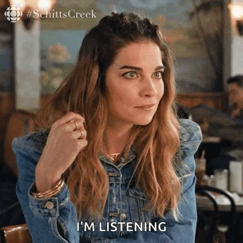 a woman in a denim jacket is sitting at a table and says i 'm listening