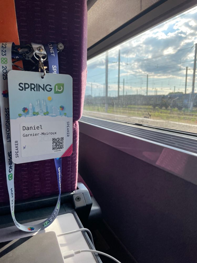 View from inside a French high speed train. Daniel’s spring io badge is dangling from the seat. In the background, a train yard view through the train window.