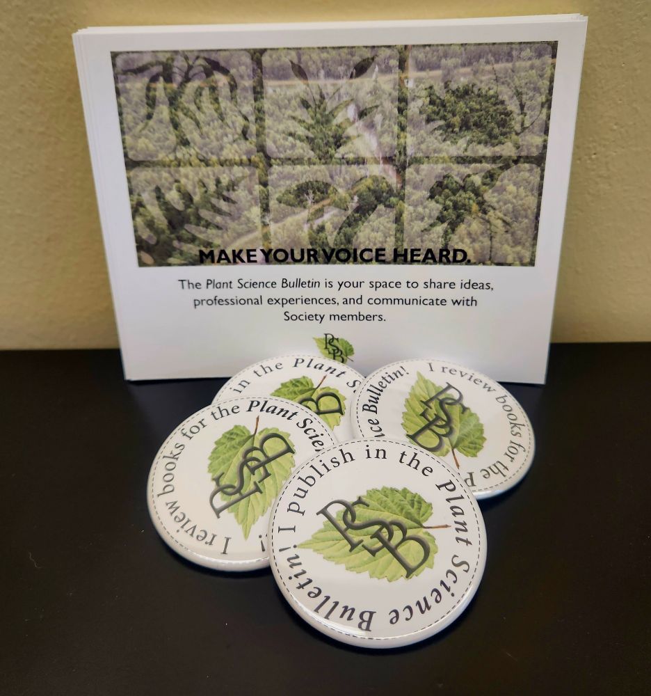 Photo of a table. In it there are postcards that say "Make your voice heard. The Plant Science Bulletin is your space to share ideas, professional experiences, and communicate with Society members". In front of the postcards, there are four buttons that say "I publish in the Plant Science Bulletin" and "I review books for the Plant Science Bulletin".
