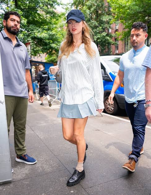 taylor swift wearing a cap white striped shirt blue skirt and loafers