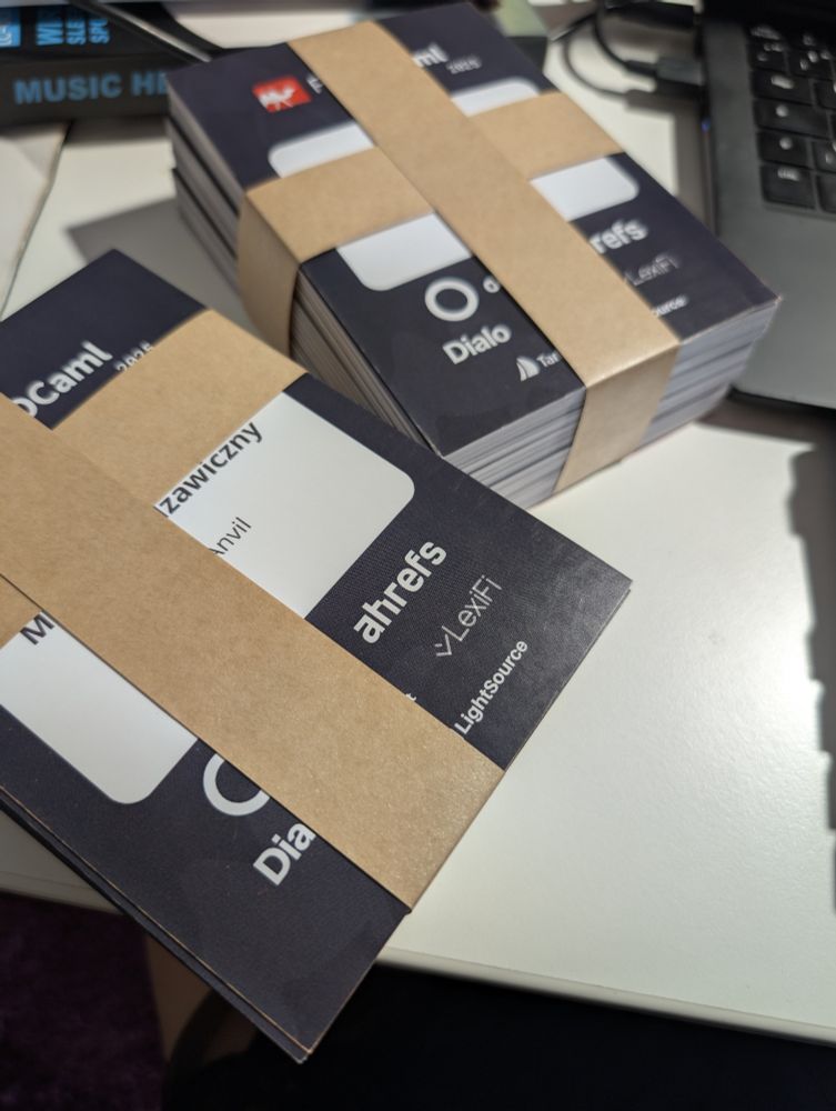 Some kind of cards with modern design featuring black backgrounds and beige/tan colored bands across the middle. The cards display names including "Zawiczny" and partial text showing "Dialo" and "ahrefs" branding. Multiple stacks of cards are arranged on a white surface next to a laptop keyboard. The cards appear to have a professional, minimalist aesthetic with white text on dark backgrounds and coordinating tan accent stripes.