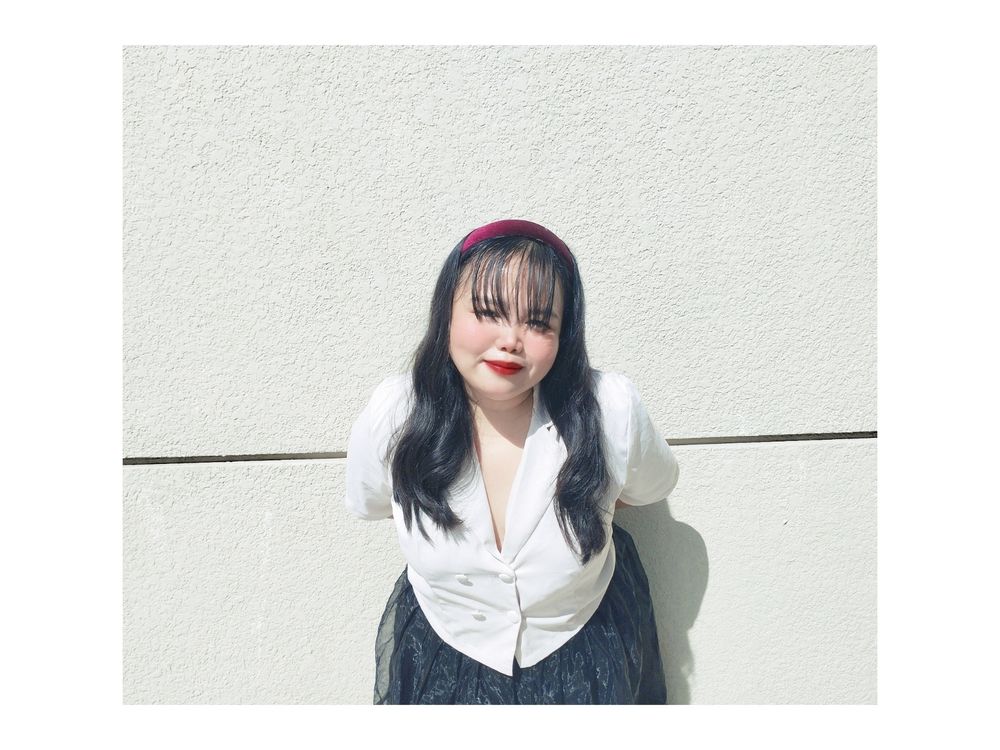 Fair skinned girl with a white open necked button down blouse, a mesh black skirt, long black hair, red headband and red lips.