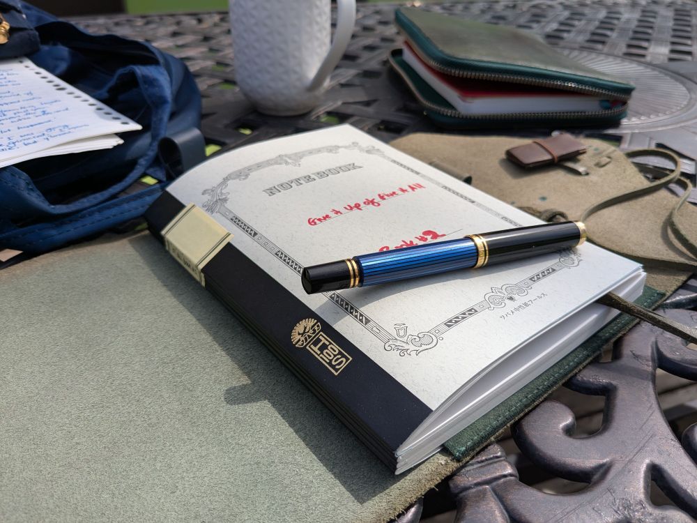 a notebook on an outdoor table, with a blue Pelikan m600 fountain pen on top. 