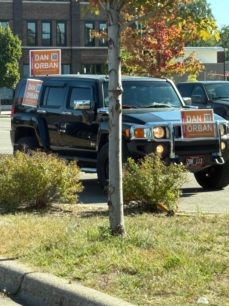 Black SUV with three Dan Orban signs taped to the front, side, and back 