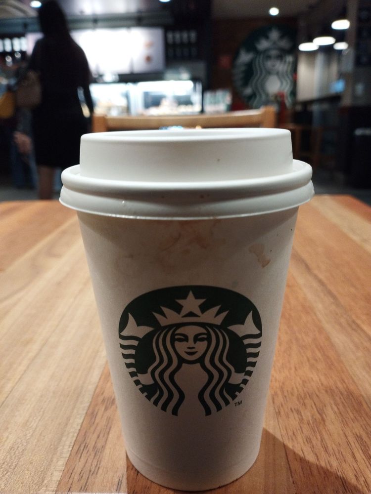 Um copo de café do starbucks em uma mesa de madeira com o fundo desfocado da cafeteria