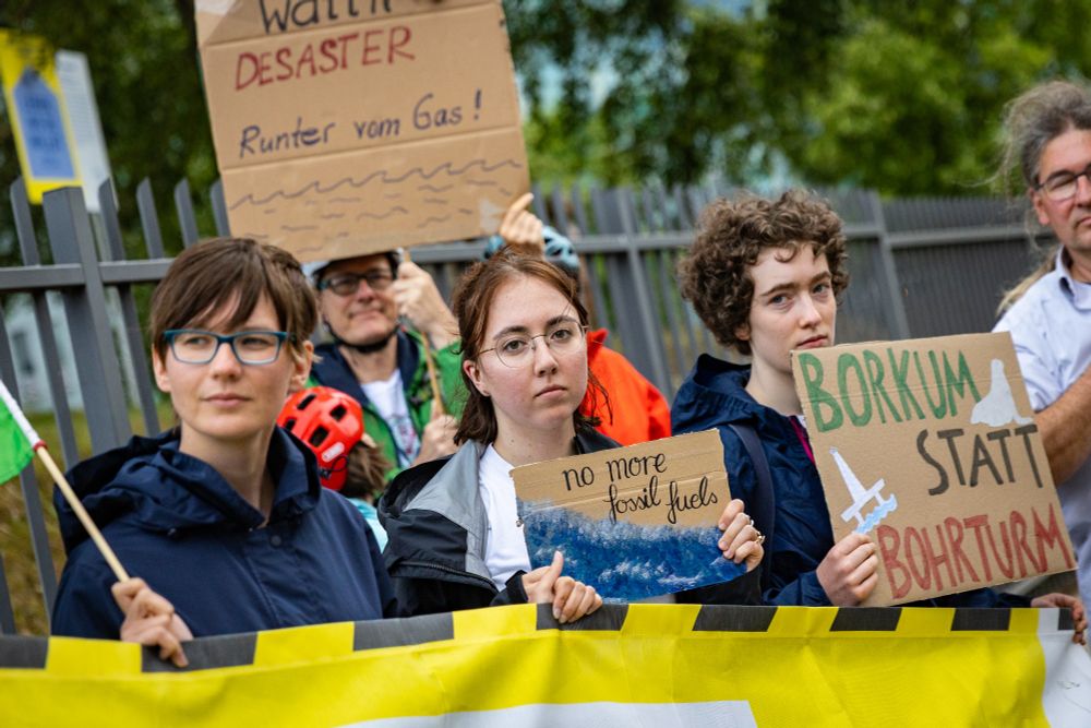 Mehrere Menschen mit Schildern gegen Gasbohrungen vor Borkum hinter einem Banner vor einem Zaun