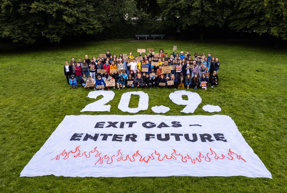 Menschen mit Pappschildern auf einer Wiese, davor die Zahlen 20.09. Und der Schriftzug Exit Gas Enter Future auf einem Banner