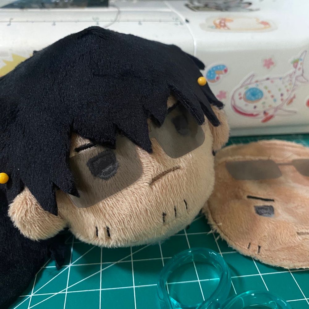 Teru Wolfwood plush head with pinned on hair and sunglasses. There are additional plush faces sitting flat on the right.