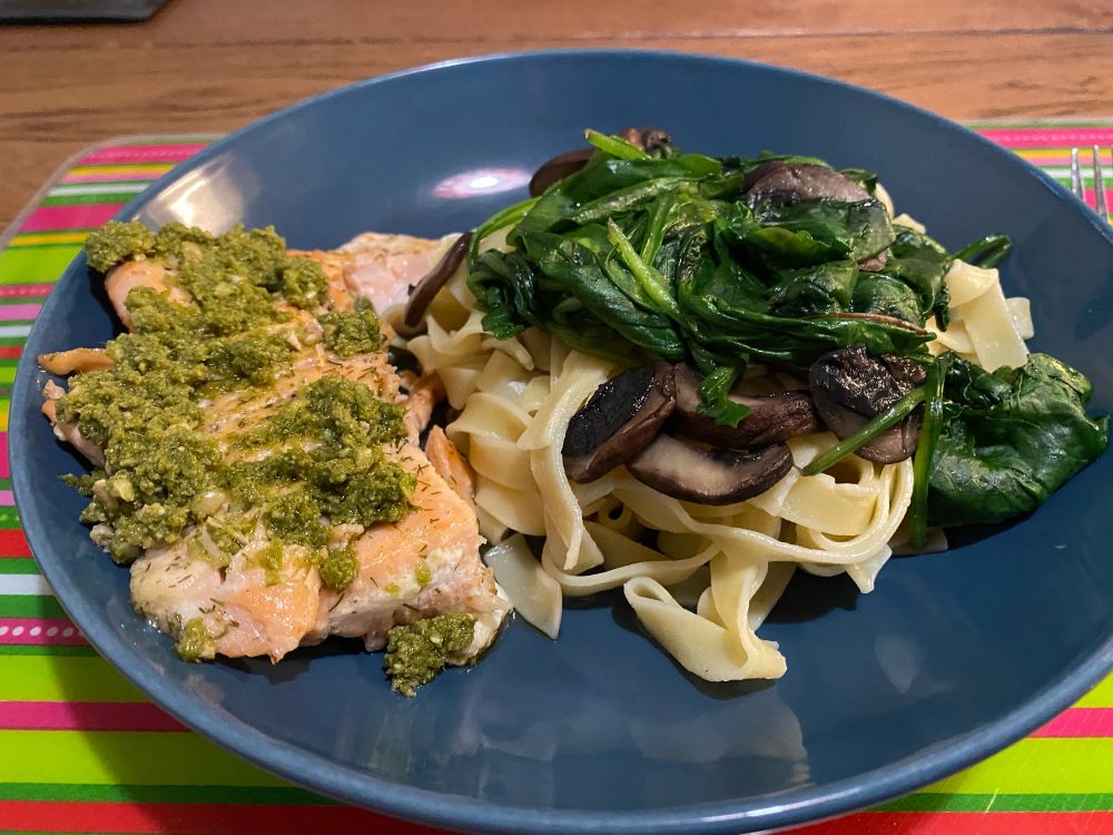 Blauw bord met daarop zalm met pesto, tagliatelle, champignons en spinazie.