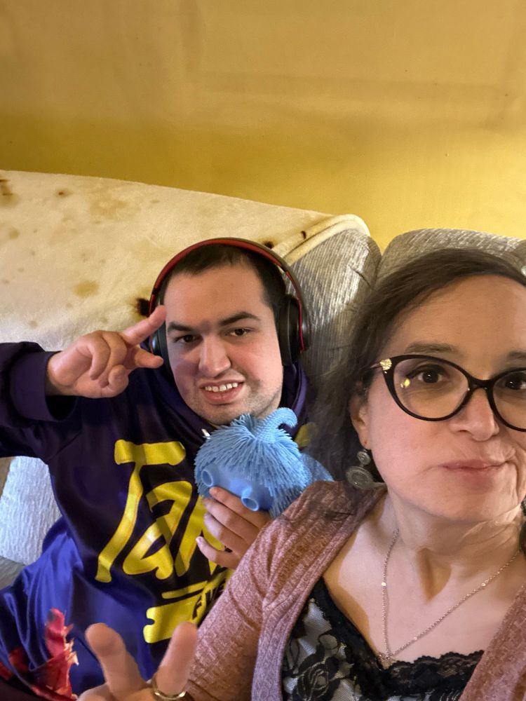 A young man doing the peace sign wearing noise cancelling headphones next to an mature woman also doing the peace sign  