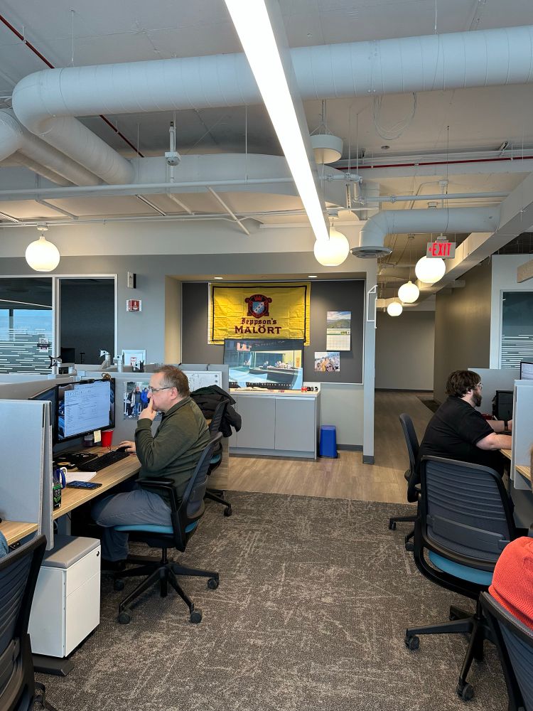 People working in the office with a malört logo on a yellow flag in the background. 