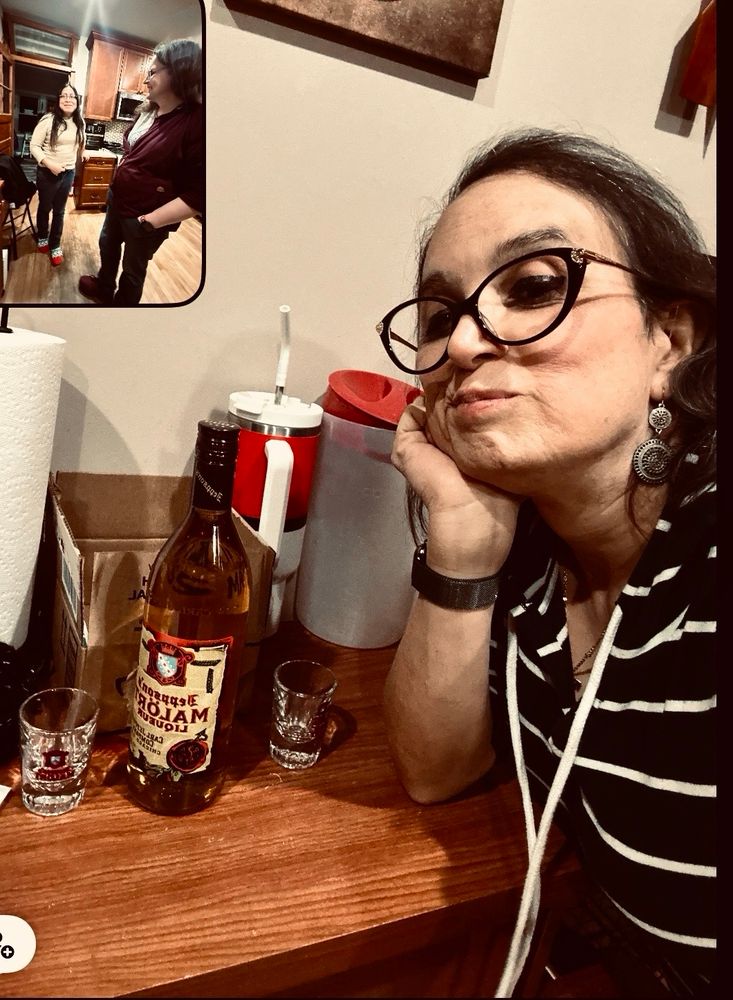 Woman posing by a bottle of Malört with two Malört shot glasses