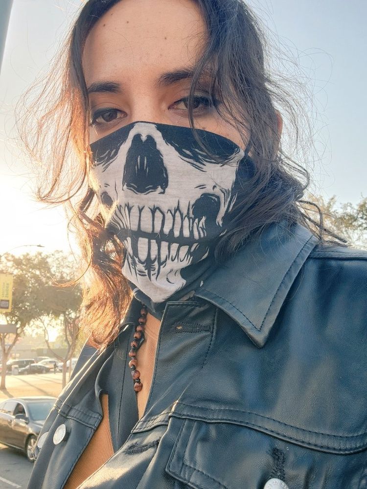 A selfie of a ghost of Eli wearing a lower half skull mask leather jacket and yellow tank top behind a sunset