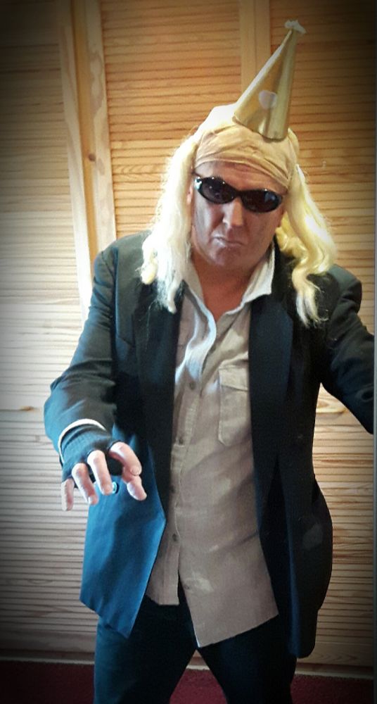 Der Klös verkleidet als RiffRaff. Schwarze Jeans, schwarzes Sakko, helles, schief geknöpftes Hemd. Weißhaarige Perücke, Partyhütchen, Sonnenbrille, Handstulpen. Silbermake-up und silberne Lippen.