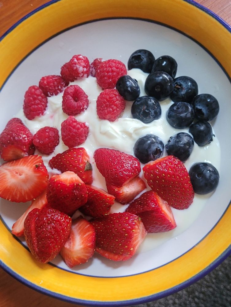 A bowl of strawberries, raspberries, and giant Blueberries on yoghurt. 