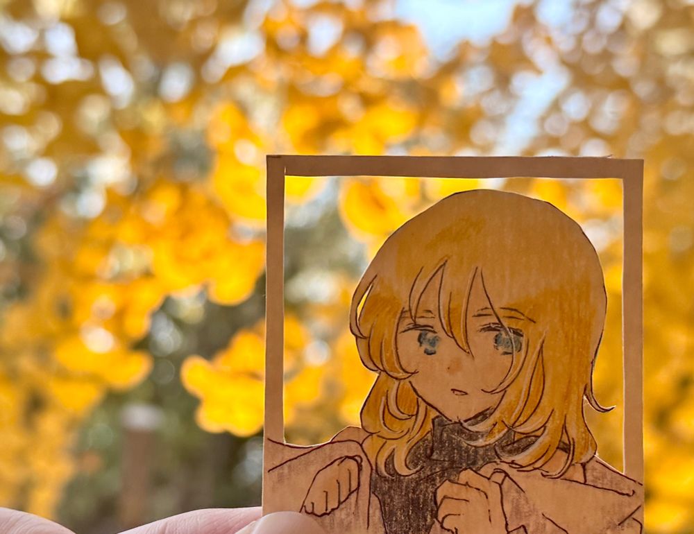 銀杏の木を背にしたレイくんのイラストの写真。イラストは背景が切り抜かれており、銀杏の葉が背景のようにも見えます。