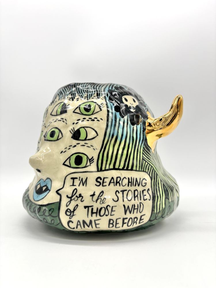Handbuilt ceramic vessel of a multi-eyed woman with gold horns saying: I’m searching for the stories of those who came before