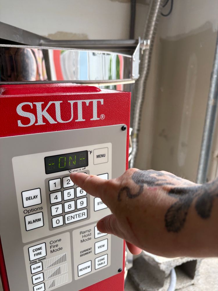 White tattooed hand pointing to the skutt kiln computer reading ON. 