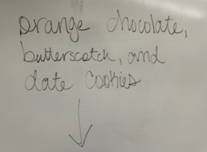 The words, "orange chocolate, butterscotch, and date cookies" written on a white board. 