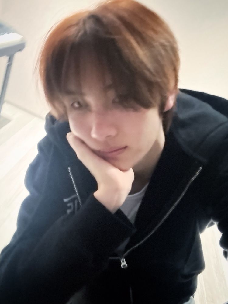 Youngjae blurry selfie in black hoodie over white t-shirt, with hand on cheek