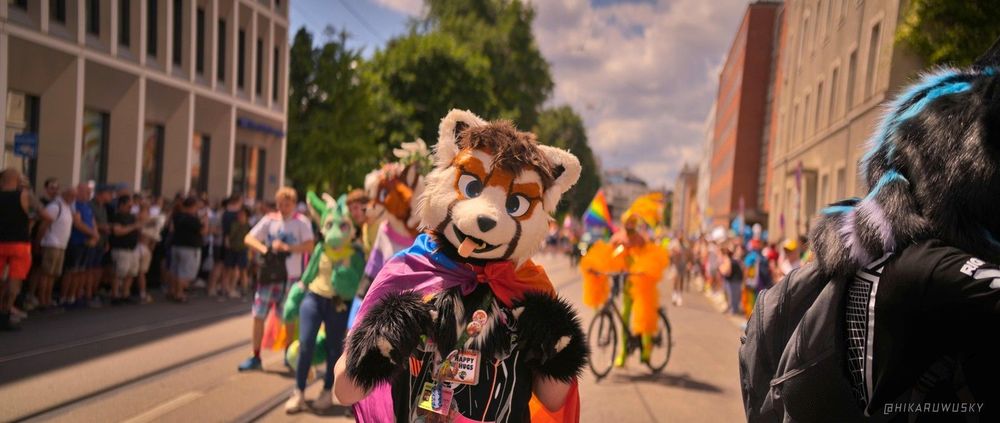 Me in partial suit with a pride flag I wear as a cape.