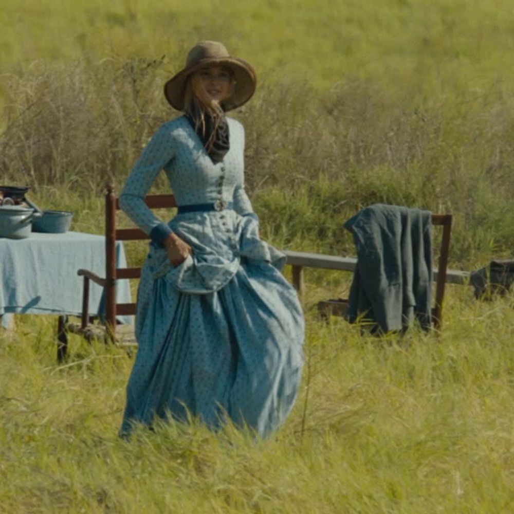 a woman in a blue dress and hat stands in a grassy field