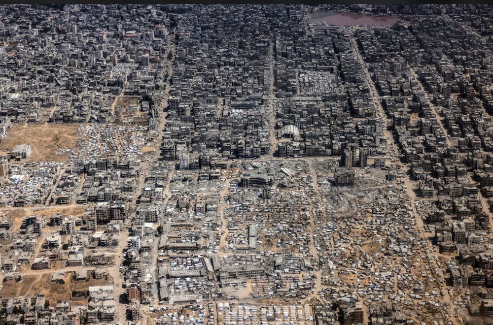 Whole area that used to be houses, shops, public transport routes, made into rubble and blackened, unliveable ruins. Aerial shot shows vast area entirely obliterated as habitable, attacked again and again by Israeli forces. 