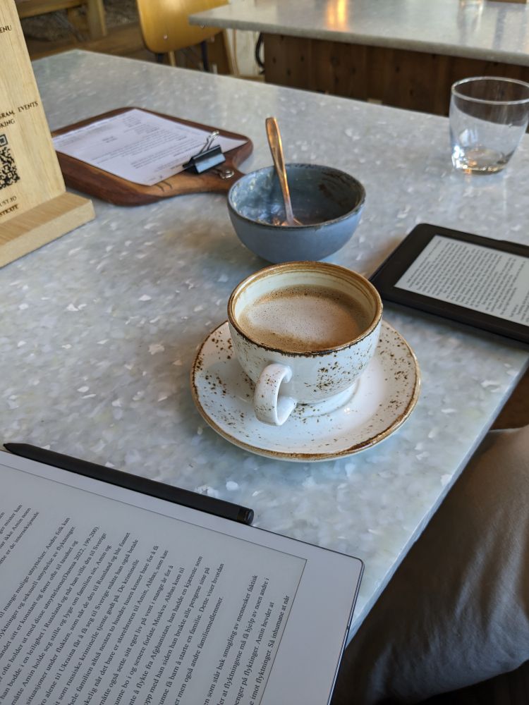 Et kafébord i stein med en kaffekopp og tom skål. Det er en reMarkable og en Kindle på bordet. 