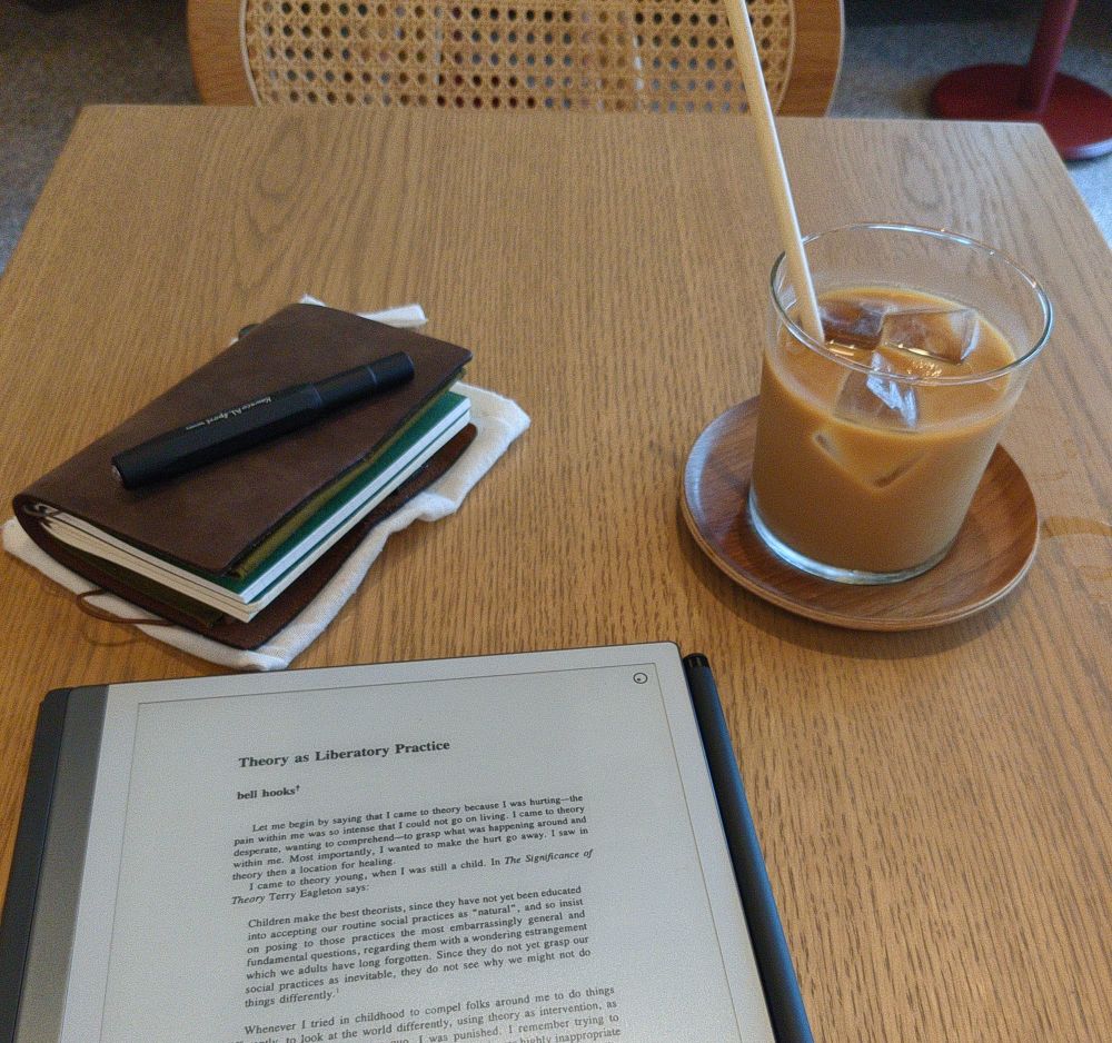 Et lesebrett, almanakk og islatte på et kafébord. Glasset står på en bordbrikke i tre.