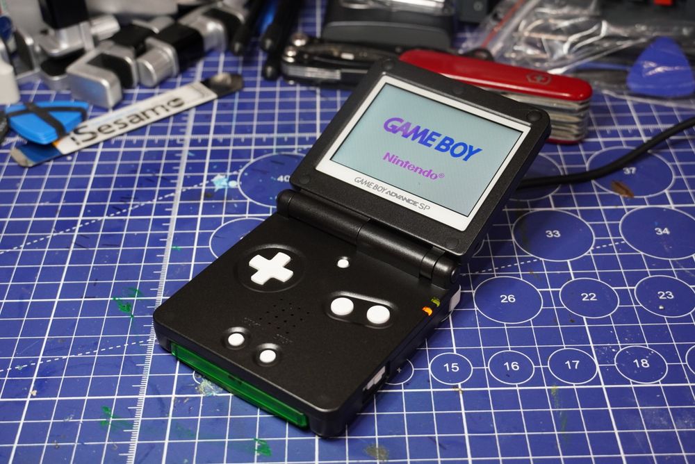 Money Shot of a Black Gameboy Advance SP with white buttons and bezel, showing the Gameboy splash screen.