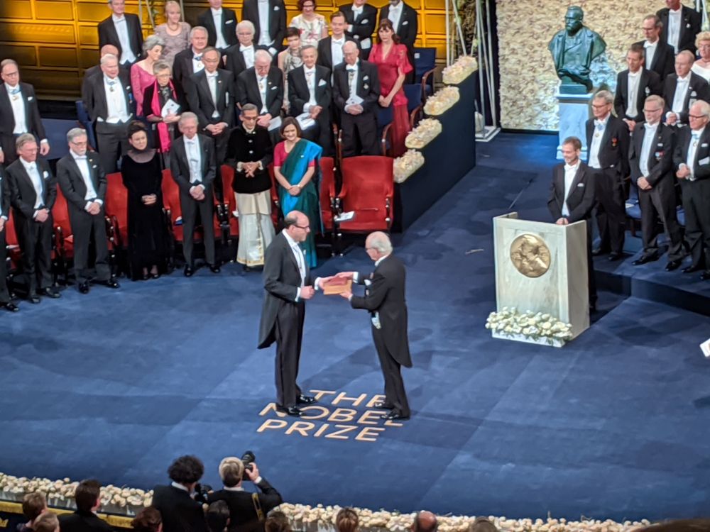 Michael Kremer received the 2019 Nobel Prize in Economic Sciences along with Abhijit Banerjee and Esther Duflo for developing an experimental approach to alleviating global poverty. Their work involved designing targeted field experiments to find effective solutions for issues like child health and education deficiencies, leading to widely adopted anti-poverty programs and policies. This photo shows Kremer receiving the prize from the King of Sweden, Carl XVI Gustaf.