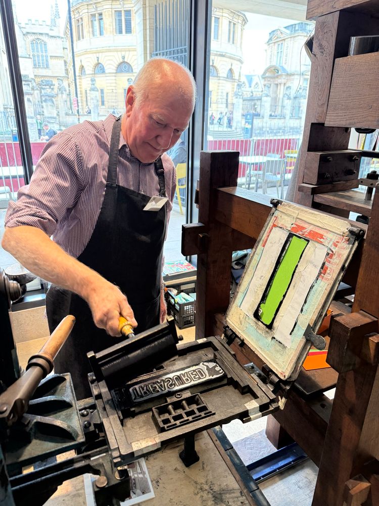 A man rolls paint onto a metal plate to print the word “Treasured”. 