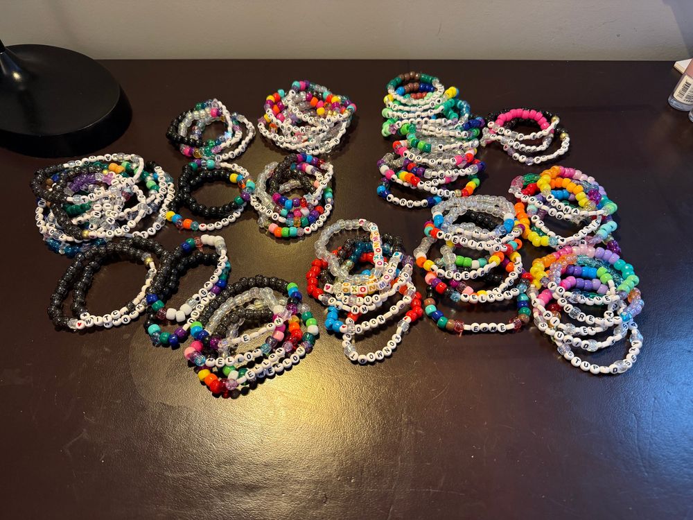73 friendship brackets made from brightly colored pony beads laying in piles on a brown desk. 