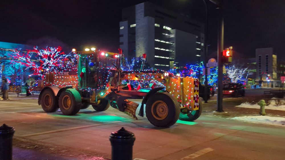 Road grader covered in Christmas lights on a City street at night time.