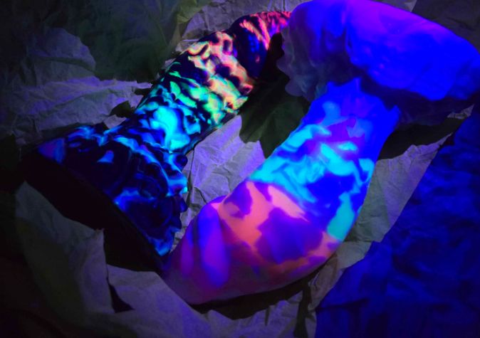 Rainbow swirl in black glitter poured in Bad dragon model crackers with rainbow swirl in a light color pour the same as crackers both laying side by side 69 under UV light