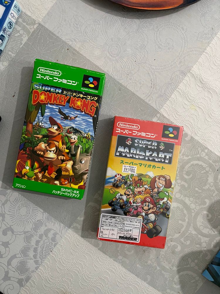 Deux boîtes de jeux Super Famicom. Super Donkey Kong ou Donkey Long Country et Super Mario Kart. 
La boîte de Super Mario Kart est encore emballée et bénie d’un filtre anti propagande de Jarm0u. 