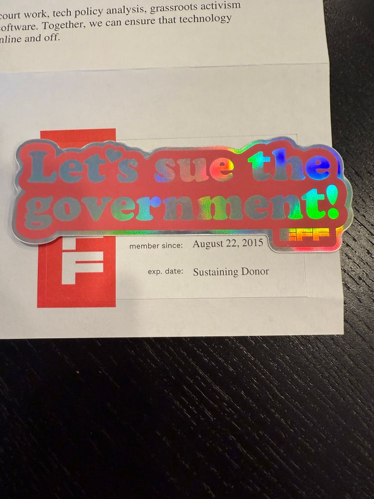 Photo of EFF membership letter showing I’ve been a member since August 22, 2015. Covering my name and member number is their new sticker, which reads “Let’s sue the government!”