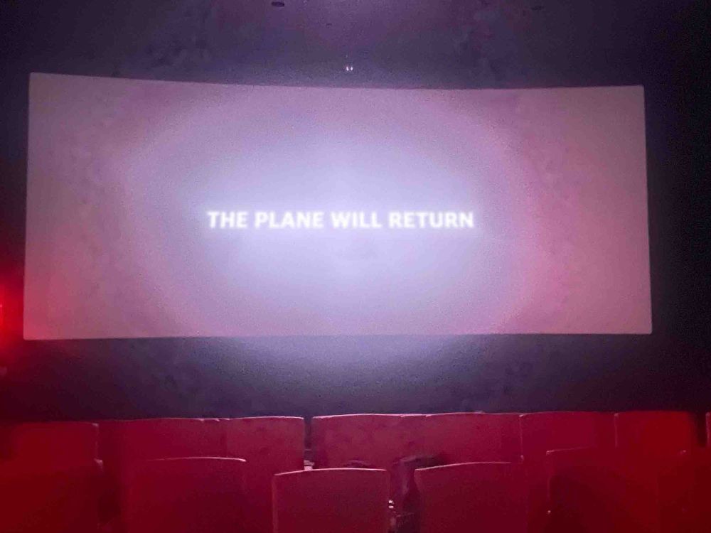 Terrible photo of the end credits of Plane (2023) in a movie theater. The screen says “The Plane Will Return.”